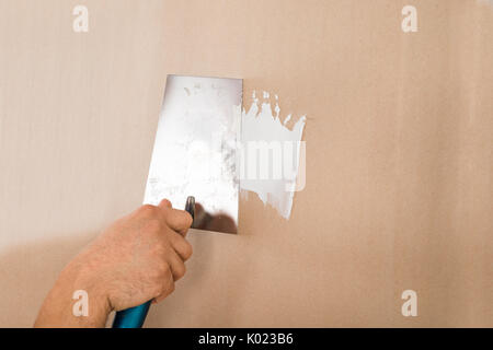 Ritagliate la mano di uomo con coltello da stucco sulla parete marrone a casa Foto Stock