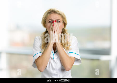 Disperato e sconvolto giovane infermiere. La donna sorpresa in bianco uniforme guardando spaventato e inorridito su sfondo sfocato. Foto Stock