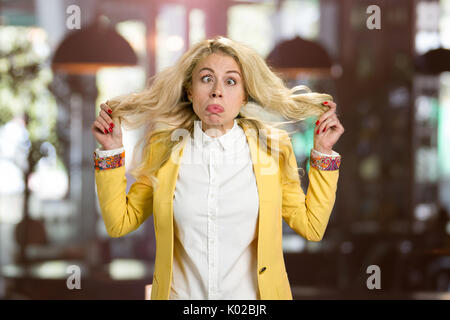 Giovane donna bionda rendendo grimace. Giovane donna rendere divertente faccia su sfondo sfocato. Foto Stock