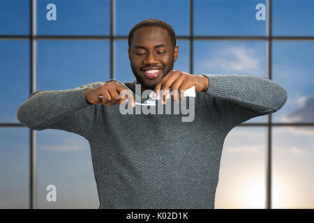 Uomo nero applicando il dentifricio sullo spazzolino. Sorridente afro-americano con il dentifricio e spazzola sul cielo blu sullo sfondo. Con la cura della salute per via orale Foto Stock