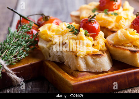 Bruschetta con uova strapazzate e cotta a forno e pomodori ciliegini, delizioso antipasto estivo Foto Stock