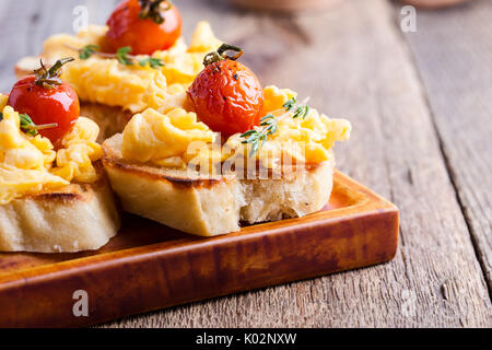 Bruschetta con uova strapazzate e cotta a forno e pomodori ciliegini, delizioso antipasto estivo Foto Stock