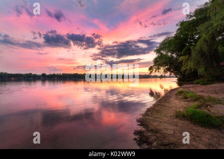 Tranquillo paesaggio con fiume e colorato il cielo con le nuvole al tramonto. Un paesaggio fantastico con il lago, spiaggia, red sky con multicolore nuvole riflettono in wa Foto Stock