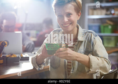 Ritratto sorridente ingegnere femmina montaggio circuito stampato in officina Foto Stock