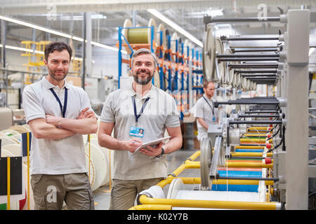 Ritratto sorridente, fiduciosi i lavoratori di sesso maschile con tavoletta digitale su fibra ottica fabbrica Foto Stock