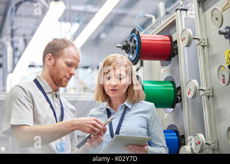 Lavoratori di sesso maschile e di sesso femminile con tavoletta digitale esaminando parte della fibra ottica factory Foto Stock