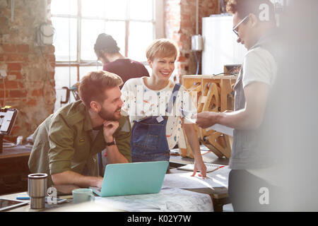 Riunione di progettisti, discutendo piani a laptop in officina Foto Stock