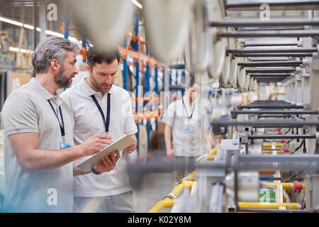 Supervisore di sesso maschile e lavoratori con appunti parlando in fibre ottiche factory Foto Stock