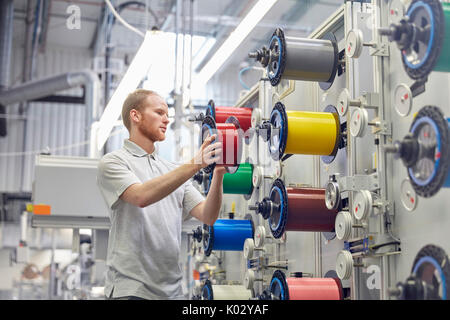 Lavoratore di sesso maschile modifica rocchetti sui macchinari in fibre ottiche factory Foto Stock