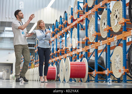 Maschio e femmina i supervisori di controllare l'inventario in fibre ottiche factory Foto Stock