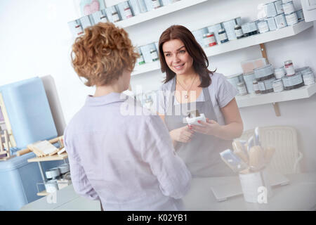 Femmina proprietario di business utilizzando il lettore di carte di credito, aiutando il cliente a contatore in arte Paint shop Foto Stock