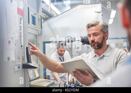 Supervisore maschio con appunti utilizzando macchinari nel pannello di controllo in fabbrica Foto Stock