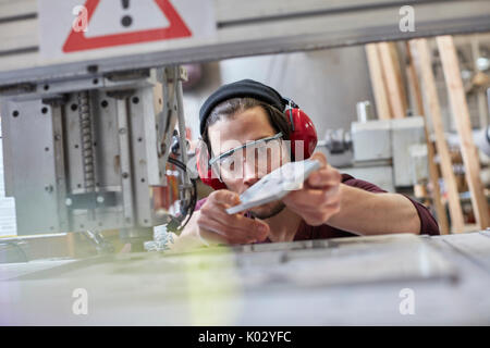 Designer maschio indossare protezioni per le orecchie, esaminando il prototipo in officina Foto Stock