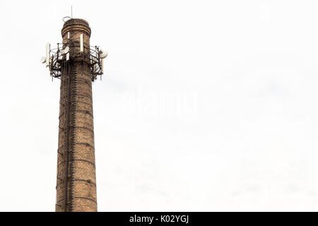 Vecchia ciminiera in mattoni con le antenne su sfondo con cielo nuvoloso Foto Stock