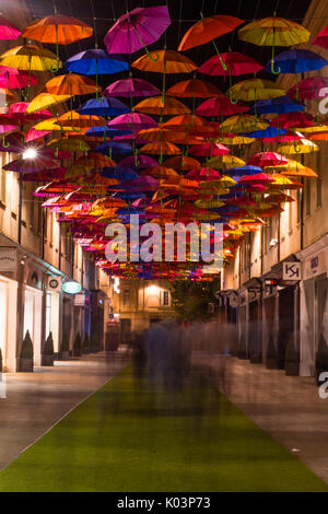 BATH, Regno Unito - 19 ago 2017 acquirenti e ombrelloni su San Lorenzo Steet. Arte pubblica installazione su strada dello shopping con molte persone a piedi di notte Foto Stock