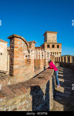 Vigoleno, Piacenza, Emiglia-Romagna, Italia. Donna in piedi sulle mura del castello cercando la città sottostante. Foto Stock