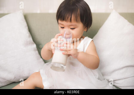 Carino bambina bere latte con baffi di latte a casa Foto Stock