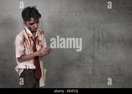 Scary asian zombie uomo azienda cellulare oltre il muro sporco sullo sfondo Foto Stock
