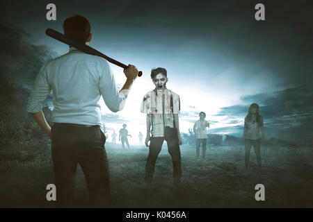Vista posteriore del uomo asiatico tenendo mazza da baseball contro gli zombie sulla campagna spaventoso Foto Stock