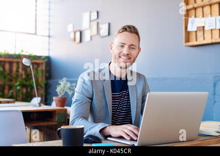Sorridente giovane imprenditore lavora su un computer portatile in un ufficio Foto Stock