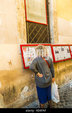 Donna che legge l'unita sul display al di fuori della locale sezione pci nel centro storico della città di Roma Foto Stock