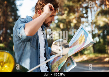 Immagine del bel giovane uomo barbuto vicino a scooter guardando la mappa all'esterno. Foto Stock