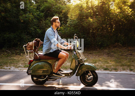 Immagine di grave giovane uomo barbuto su scooter all'esterno. Guardando a parte. Foto Stock