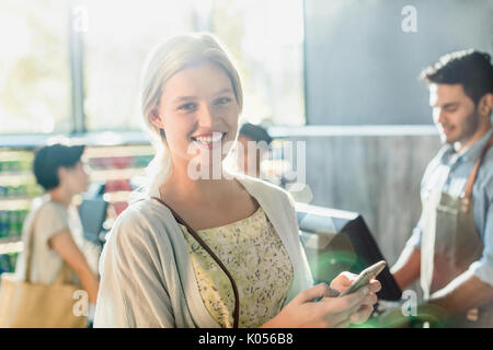 Ritratto sorridente ragazza con un telefono cellulare al negozio di alimentari checkout Foto Stock