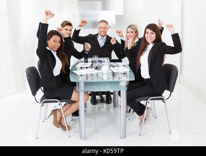Ritratto di business di successo di squadra con bracci sollevati seduto alla scrivania in ufficio Foto Stock
