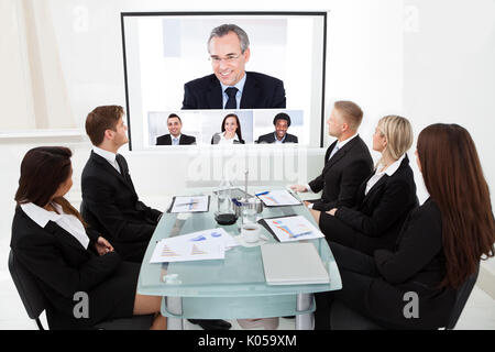 Gli imprenditori guardando lo schermo del proiettore in video-conferenza in ufficio Foto Stock