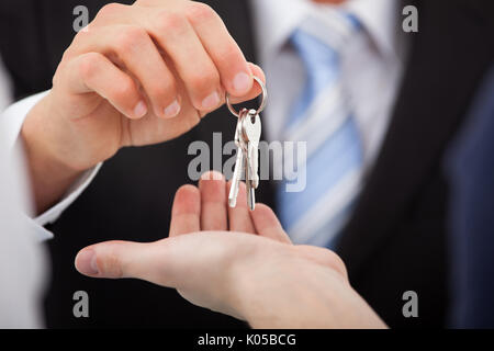 Immagine ritagliata di agente immobiliare di dare le chiavi di casa a uomo in ufficio Foto Stock