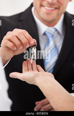 Immagine ritagliata di agente immobiliare di dare le chiavi di casa a uomo in ufficio Foto Stock