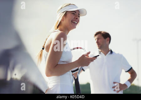 Ridendo di tennis femminile giocatore in possesso del telefono cellulare e di racchetta da tennis Foto Stock