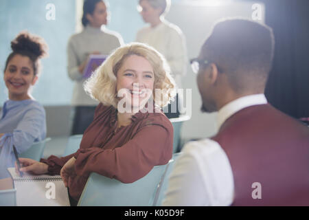 Sorridente imprenditrice di tornitura e ascolto di imprenditore nel pubblico di conferenza Foto Stock