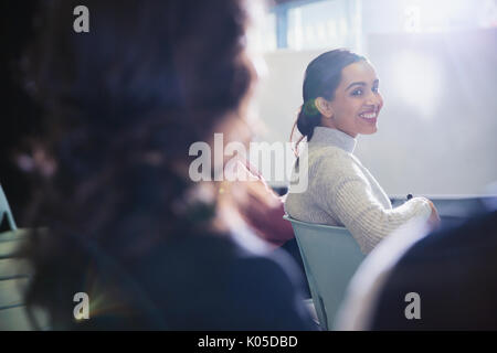 Sorridente imprenditrice di tornitura, guardando indietro nel pubblico di conferenza Foto Stock