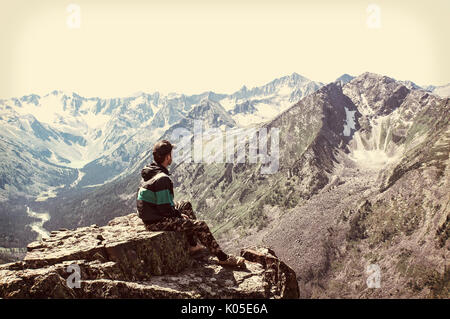 Uomo seduto sulla scogliera affilato al di sopra della valle di montagne rocciose park e guardare nel paesaggio. Il turista ha conquistato la cima della montagna e si siede godere Foto Stock