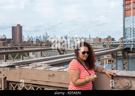 Una donna prende un selfie con un bastone sul ponte di Brooklyn a New York City, Stati Uniti d'America. Foto Stock