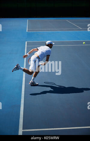 Tennis maschile giocatore giocare a tennis su blu soleggiato Campo da tennis Foto Stock