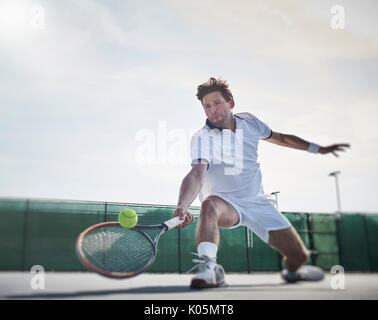 Determinato maschile giovane giocatore di tennis giocando a tennis, raggiungendo per la palla sul soleggiato Campo da tennis Foto Stock