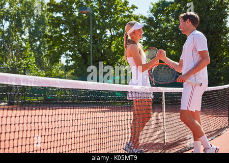 Maschio e femmina i giocatori di tennis fist bumping al netto sul soleggiato Campo da tennis in terra battuta Foto Stock