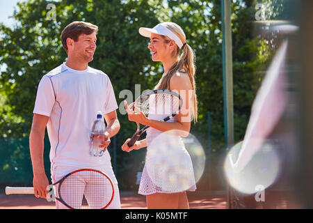 Sorridente maschio e femmina i giocatori di tennis a parlare e tenendo le racchette sul soleggiato Campo da tennis Foto Stock