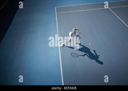 Vista aerea femmina giovane giocatore di tennis giocando a tennis, colpendo la palla sul blu soleggiato Campo da tennis Foto Stock