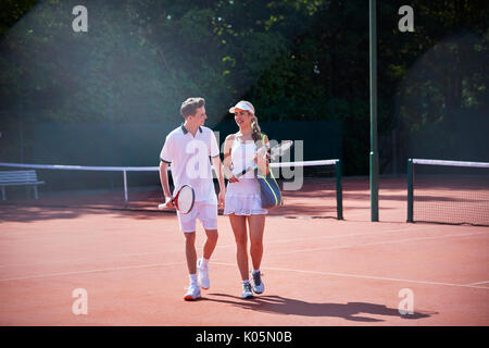 Giocatore di Tennis giovane camminare portando racchette da tennis sul soleggiato Campo da tennis in terra battuta Foto Stock