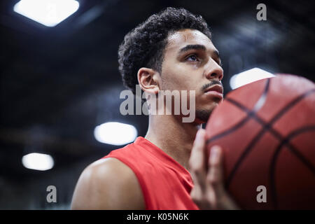 Ritratto di grave, focalizzata maschile giovane giocatore di basket tenendo la pallacanestro Foto Stock