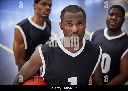Ritratto di grave, focalizzata maschile giovane giocatore di basket team indossare maglie nero Foto Stock