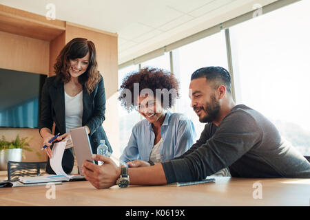 Multirazziale la gente di affari con tavoletta digitale avente riunione in ufficio. La gente di affari guardando il computer tablet e sorridente. Foto Stock