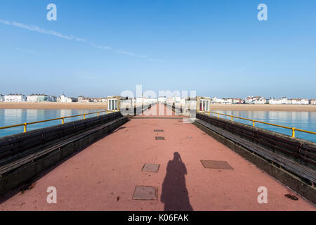 Ampio angolo di visione di trattare Pier dalla fine del molo centrata nel centro guardando indietro alla calma alba mare, spiaggia e la città in lontananza. Foto Stock