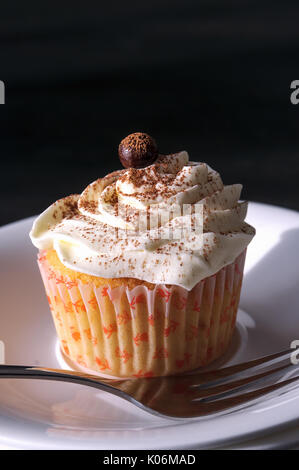 Il tiramisù cupcake su una piastra con una forchetta. Sul tavolo. Cioccolatini e rabboccato.; angel food cupcake e crema di mascarpone. Sfondo scuro. Nel taglio. Foto Stock
