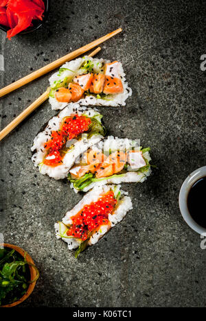 Trend alimentari ibrido. Giapponese cucina asiatica. Mini sushi-tacos, panini con salmone, hayashi wakame, daikon, zenzero, caviale rosso. Nero tavolo di pietra, wi Foto Stock