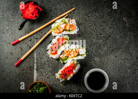 Trend alimentari ibrido. Giapponese cucina asiatica. Mini sushi-tacos, panini con salmone, hayashi wakame, daikon, zenzero, caviale rosso. Nero tavolo di pietra, wi Foto Stock
